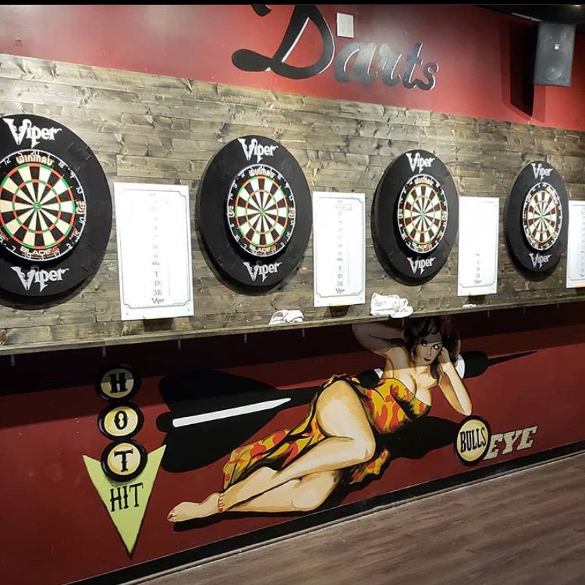 Five dart boards in a row on the wall under the word Darts, with a painted figure below them.