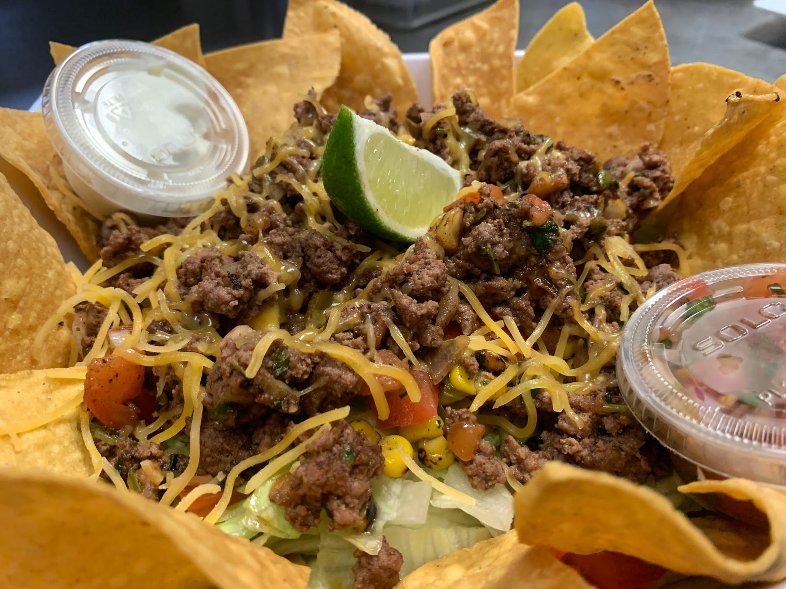 A taco salad in a tortilla bowl with seasoned beef, shredded cheese, lime and sour cream.