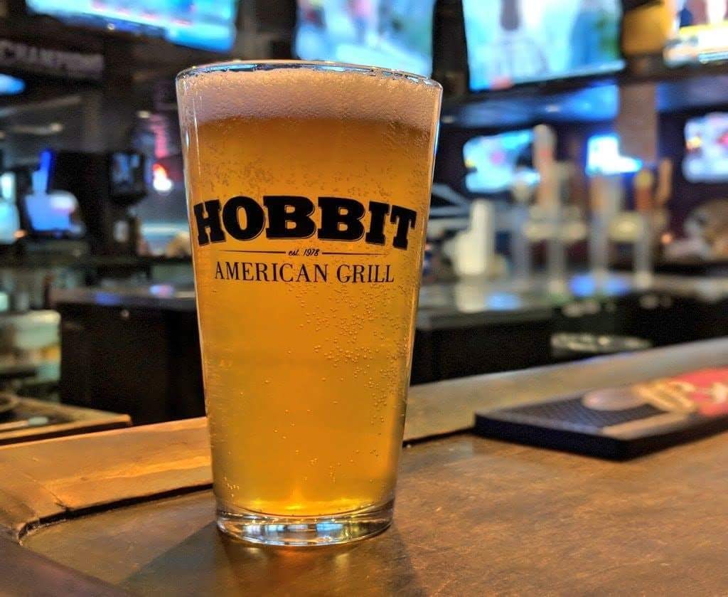 A full pint glass printed with the Hobbit American Grill logo, on the bar.
