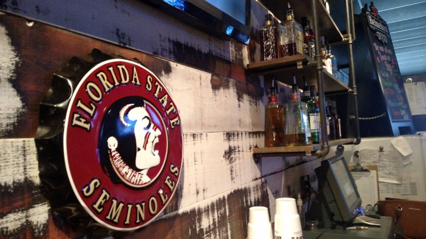 A round Florida State Seminoles sign mounted on the wood wall above the bar.