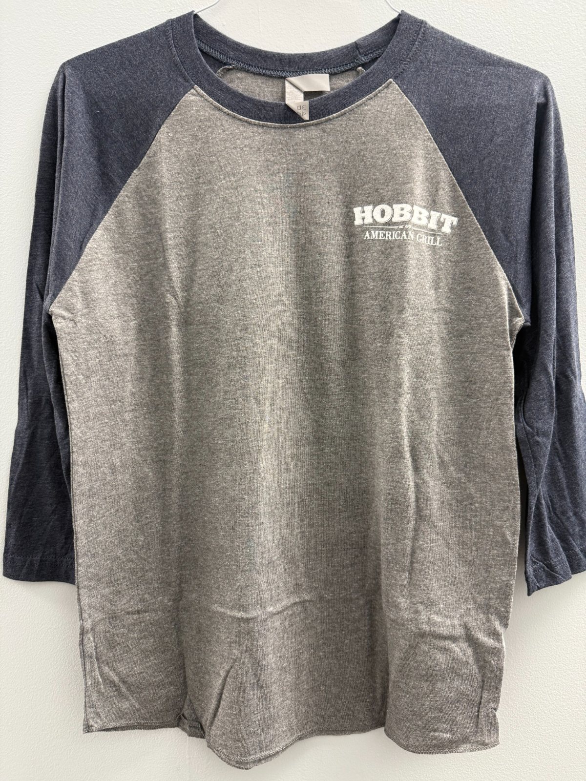 The front of the grey and navy 3/4 sleeve baseball shirt with a small Hobbit American Grill logo on the chest.