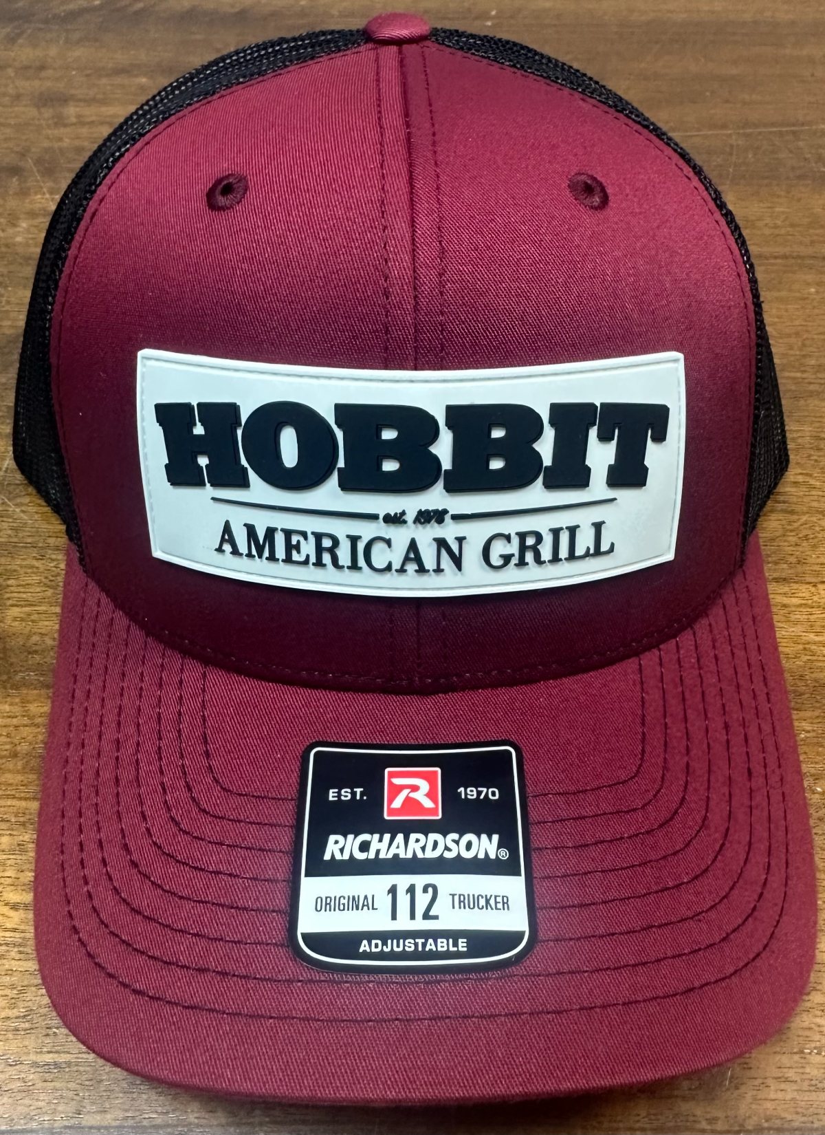A garnet and black mesh-back cap with a white Hobbit American Grill patch on the front.